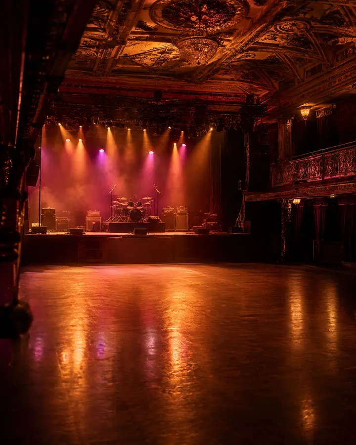 Empty music hall stage lit in amber and magenta under an ornate ceiling